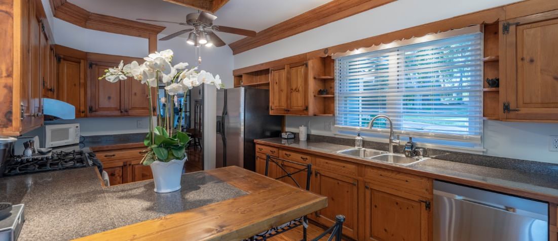 Kitchen with stainless steel appliances, oak cabinets, ceiling fan with light fixtures, vase with silk arrangement, microwave in corner.